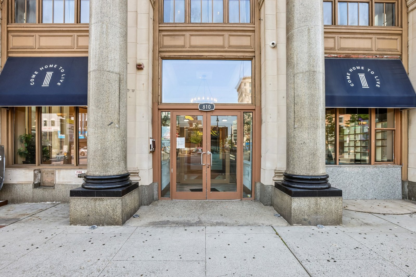 Glass entrance doors marked 810 between stone columns and navy awnings.